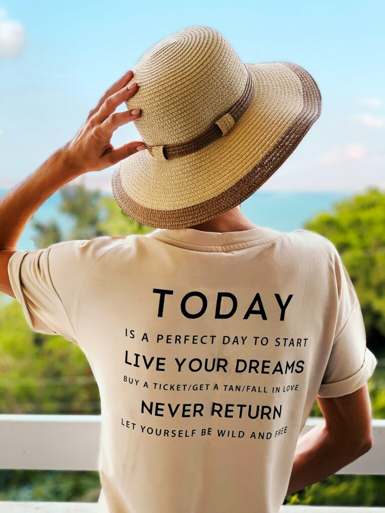 young woman in summer hat and shirt with motivational phrase standing in front of tropical nature